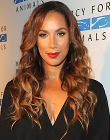 A woman with long, curly brown hair looking directly forward, wearing a black outfit, and red lipstick.