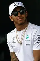 A black man in his early thirties with short facial hair smiling while wearing a hat.