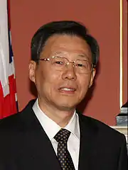 a man with a wavy haircut, wearing glasses, a white shirt, a suit and a black tie with white dots