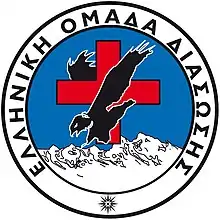 The Hellenic Rescue Team crest, a black eagle in front of a red cross, over white mountains.