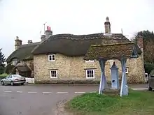 Cast iron pump with its own tiled roof. Behind are two stone built thatched cottages.