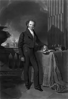 Engraved full-length portrait of a balding man standing next to a table with his left arm resting on a book and in the background a stone balustrade beyond which are trees and a building with columned portico