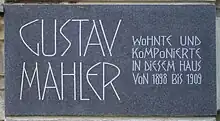 A dark plaque with white lettering in which the composer's name is shown in extra large characters on the left, the main message in smaller characters on the right