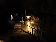 A boat moored beside a concrete path on an underground lake, with darkness surrounding.