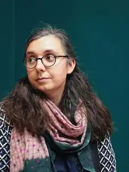 A woman with glasses and greying brown hair looking to the left