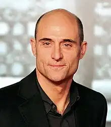 A head-and-shoulders view of a bald middle-aged Strong, wearing a dark shirt and black jacket.