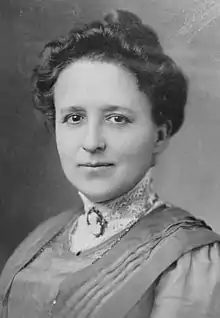 Head and shoulders of a serious and dignified woman in her forties, with dark hair up and in a dress with high lace collar and a cameo at her throat, Edwardian style