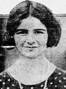 A white teenaged girl with dark hair cut in a bob and parted center, smiling, wearing a polka-dot dress with a strand of beads