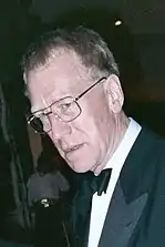 A long-faced man in a suit; he wears spectacles and his short-cropped hair is greying at the edges.