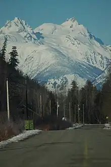 A multi-peak mountain raising above trees and a paved road