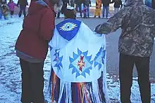 A colour photograph of a young girl in a traditional shawl between two adults