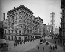 A tall, imposing stone building in an almost empty city street with tramcar passing. A tower in the background is the only other highrise building.