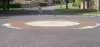 A mini-roundabout in the UK, where a painted white circle is used as centre. The arrows show the direction of traffic.