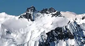 A dark rugged mountain towering over glacial ice and rock on a clear day.