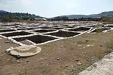 an archaeological excavation at moza. General view of an area with a semi oblique perspective showing mostly square excavation trenches arranged in a checkerboard pattern in a mediterranean landscape.