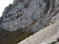 Hiker crossing scree at the foot of a mountain.