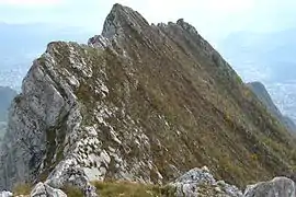 Rocky ridge with cliffs on the left and a steep slope with low vegetation on the right.