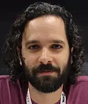 A 36-year-old man with curly black hair smirking at the camera.