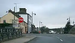 A picture of the Main Street in Newbliss, featuring the junction between the R183 and R189. Road signs for Monaghan, Three Mile House, and Aghabog are visible along with a stop sign.