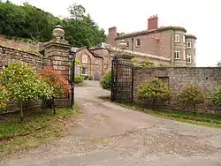 A red-brick, three-storey, historic house with a red-brick wall and gates in front