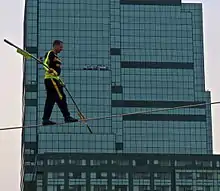 A man tightrop walks with a large building in the background