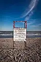 A white sign attached to a wooden structure indicating to patrons on a beach. "No Lifeguard On Duty, Call 911 in case of emergency"