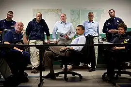 Photo of Obama listening to a briefing, surrounded by senior staffers