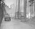 An American soldier drives past buildings set afire by survivors.