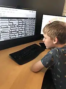 a child looking at a scanned census document and a genealogical fan chart on dual monitor computer screens in the BYU Family History Library