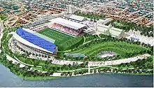 Aerial view of football field with parkland below and buildings to the right.