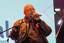 A man is wearing a black jacket and glasses and is holding a microphone