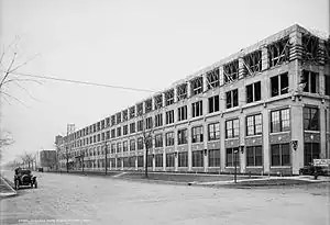 A black and white photograph of a brick building with an old car in the foreground