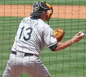 A man in a gray baseball uniform reading "Hoover" and "13" on the back and a black catcher's mask on his face throwing a baseball with his right hand