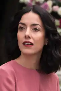 Head and shoulders image of a dark haired woman in a bright pink outfit