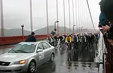 A group of bicyclist following a car.