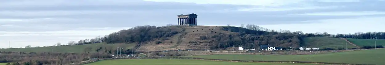 A hill partly covered in trees, with a Greek temple at the summit