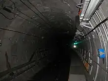 Circular concrete tunnel with cables running along the walls and a narrow emergency walkway on the right