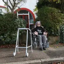 Cover art for "Boy's a Liar": an old woman in a wheelchair outside a house