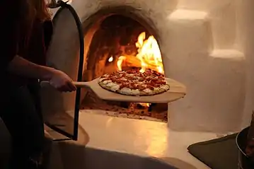 A pizza being removed with a wooden peel