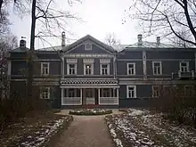 A blue two-story house with white trim and many windows, surrounded by birch trees.