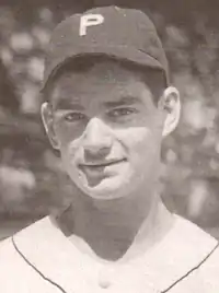 A black-and-white image of a young man in his teens shown from the shoulders up, wearing a white baseball jersey with white buttons and a baseball cap with a white block "P" on the front.