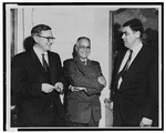 Three men standing and having a conversation. All three men are wearing suits.