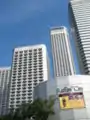 Ground-level view of the three skyscrapers, each successively taller from left to right. The towers have white facades with dark windows and a rectangular cross-section, and the building farthest to the right is the most prominent.