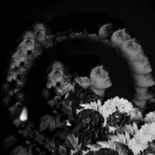 A black-and-white photograph of the duo standing with their backs to each other surrounded by flowers and a ring of blurred repetitions of their faces