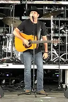 Singer Rhett Akins singing into a microphone and holding an acoustic guitar.