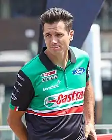 A clean shaven man in his late thirties wearing a green, black and red zip T-shirt with sponsors logos