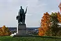 Green copper statue of a man holding a flag next to an old fashioned ballot box. Statues stands on a granite base, which has "Robert Ross" carved into it.