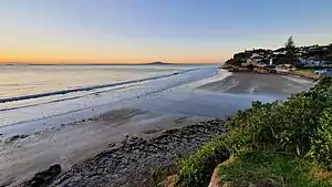 The beach at Rothesay Bay at low tide, with the Hauraki Gulf and Rangitoto in the distance