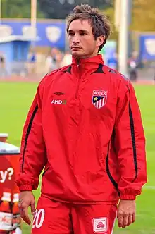 A young man with brown hair, wearing a red jacket and shorts