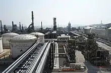 Many large metal structures, cylindrical tanks and chimneys next to a large road